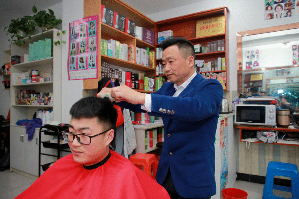 图为截肢手术半年后，胡之勤丢掉拐杖站着理发。